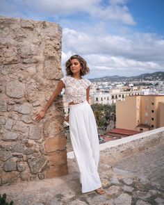 a woman leaning against a stone wall with her hands on the side and looking off into the distance