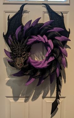 a purple and black dragon wreath hanging on a white door with a window in the background