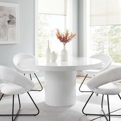 a white dining table with four chairs around it and a vase filled with flowers on top