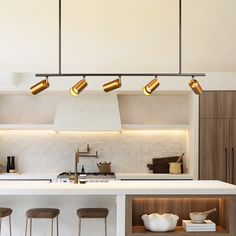 a kitchen with white counter tops and gold lights hanging from the ceiling over the island