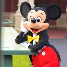 a person dressed in mickey mouse costume leaning on a table with a map behind him