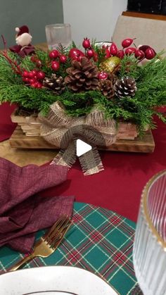 a table set for christmas with pine cones, berries and greenery in a wooden box