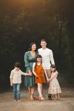 a family posing for a photo in front of some trees and bushes with the sun shining down on them