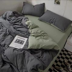 an unmade bed with grey sheets and pillows on top of it, next to a black and white checkered floor