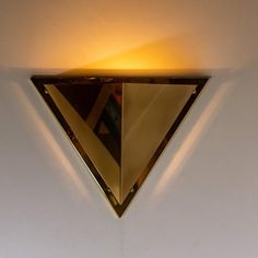 a triangle shaped mirror mounted to the side of a white wall with a light on it