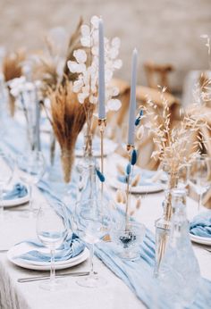 the table is set with blue and white linens, glass vases filled with flowers