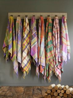 several colorful plaid towels hanging on a rack next to wood logs in front of a gray wall