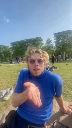 a man sitting on the ground with his hand out in front of him while wearing sunglasses