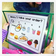 a young child holding up a poster with food and drinks on it that says may i take your order?