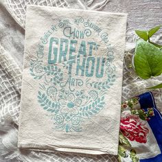 a tea towel with the words great thou on it next to a potted plant