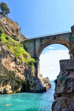 a bridge that is over water next to a cliff with a person swimming in it