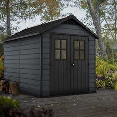 a black shed sitting on top of a wooden deck in front of some bushes and trees