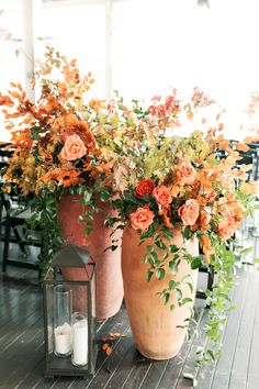 two large vases filled with flowers sitting on top of a wooden floor next to a lantern