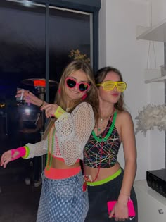 two young women dressed in colorful clothing and sunglasses posing for the camera with their arms around each other