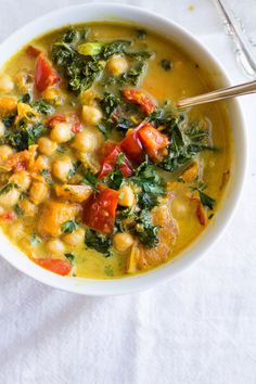 a white bowl filled with chickpeas, spinach and carrots next to a spoon