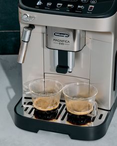 two cups of coffee being filled with liquid from an espresso machine on a counter