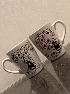 two coffee mugs with designs on them are sitting next to each other in front of a white wall