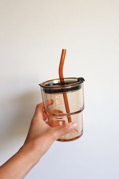 a hand holding a cup with a straw sticking out of the top, and an orange straw sticking out of it