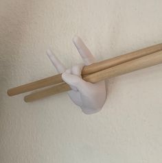 a hand holding two chopsticks up to the ceiling in front of a white wall