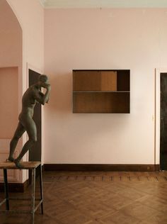 a statue is standing on top of a chair in a room with pink walls and wooden floors