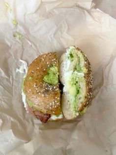 a sandwich with avocado and other toppings sitting on top of wax paper