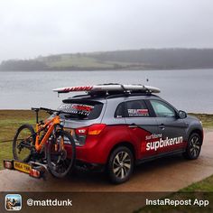 a car parked next to a lake with surfboards on the roof and bike rack