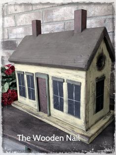 a doll house sitting on top of a wooden table next to a red rose bush