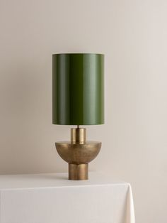 a green lamp sitting on top of a table next to a white cloth covered table