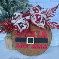 a wooden sign that says santa stop here with red and white decorations on it's side