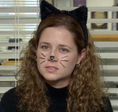 a woman with cat's head painted on her face sitting in front of a window