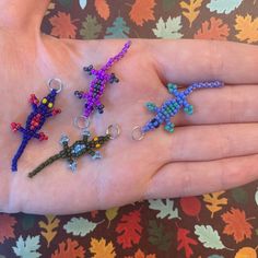 a person's hand holding five small beaded geckos in different colors