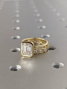 a gold ring with an emerald and diamonds on the side, sitting on top of a metal surface