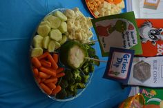 a platter of vegetables and dip sits on a blue tablecloth with signs reading dr seuss