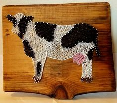 a cow made out of string on a wooden board with white and black dots around it