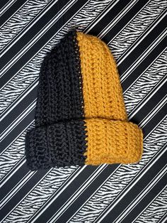 a black and yellow knitted hat laying on top of a striped table cloth,