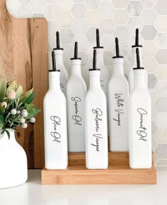 six white bottles with black writing on them sitting next to a cutting board and vase