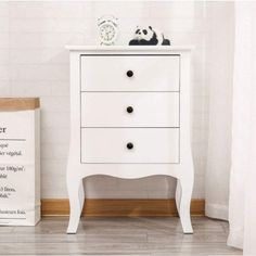 a white chest of drawers sitting on top of a wooden floor next to a clock