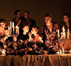 a group of people sitting at a table with candles in front of them, all dressed up