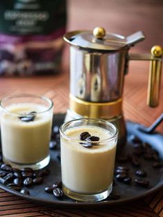 two glasses filled with coffee sit on a plate next to an espresso maker