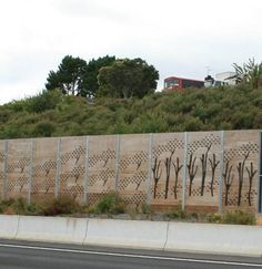 a wall with trees painted on it along the side of a road in front of a hill