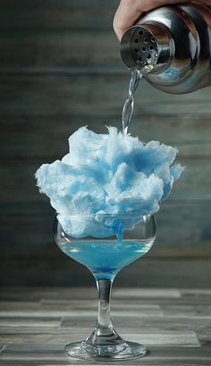 a person pours blue liquid into a martini glass filled with cotton floss and water from a faucet