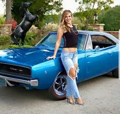 a woman standing next to a blue muscle car