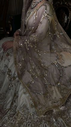 a woman in a white and gold dress sitting on a chair wearing a tiara