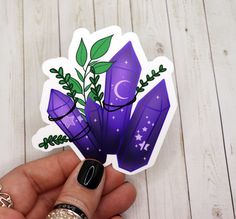 a hand holding a purple sticker with green leaves and stars on it's side