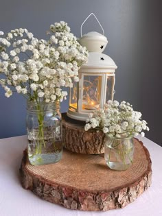 white flowers in mason jars sitting on a wooden slice with a lantern and candle behind them