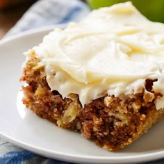 a piece of cake on a plate with white frosting and an apple in the background