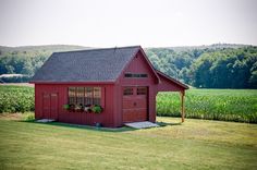 a small red barn sitting on top of a lush green field next to a corn field