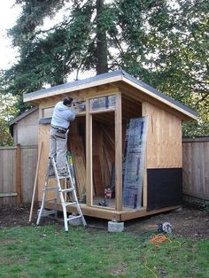 a man standing on a ladder in front of a shed that is being built into the ground