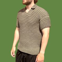 a man with a beard wearing a knitted sweater and black sweatpants, standing in front of a green background