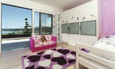 a bedroom with a pink couch and purple rug in front of large windows looking out onto the ocean